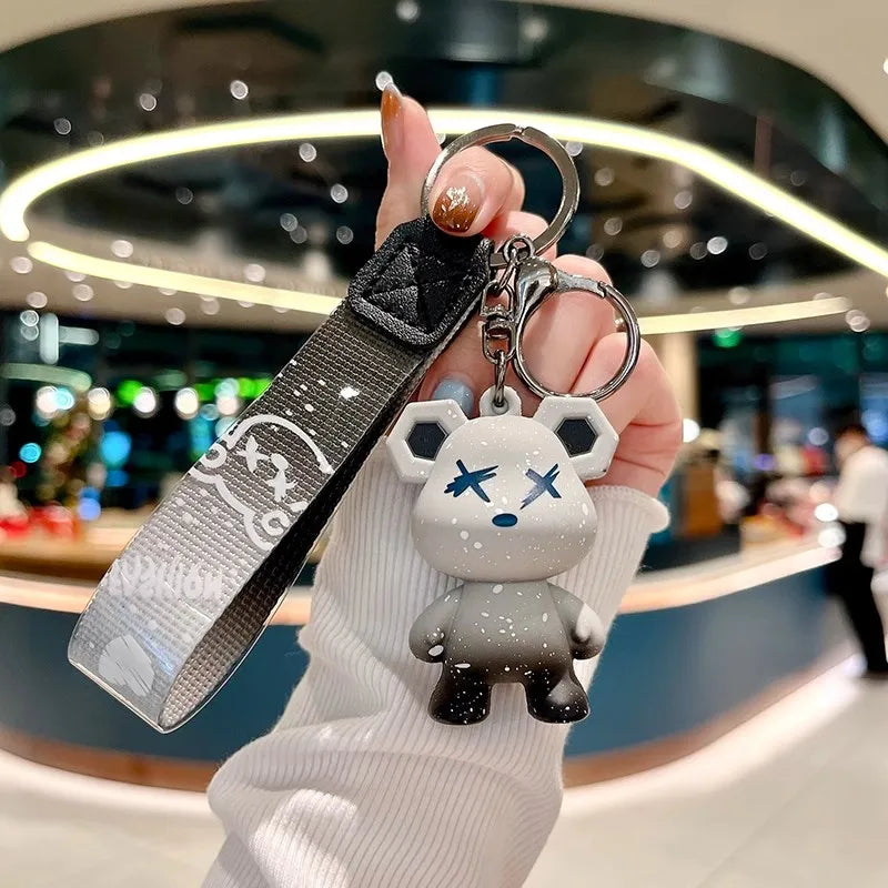 A hand holds a white bear-shaped keychain attached to a black leather key case.