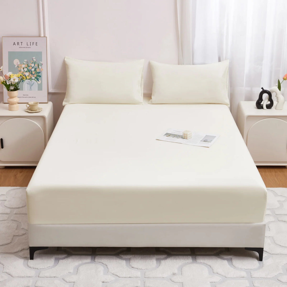 Eine cremefarbene, eng anliegende Matratzen-Schutzdecke wird auf einem Bett mit weißen Kissen und einem hellen Holzfußboden p