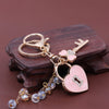 Gold-toned keychain featuring a bow and heart charm with clear rhinestones on a dark wooden surface.