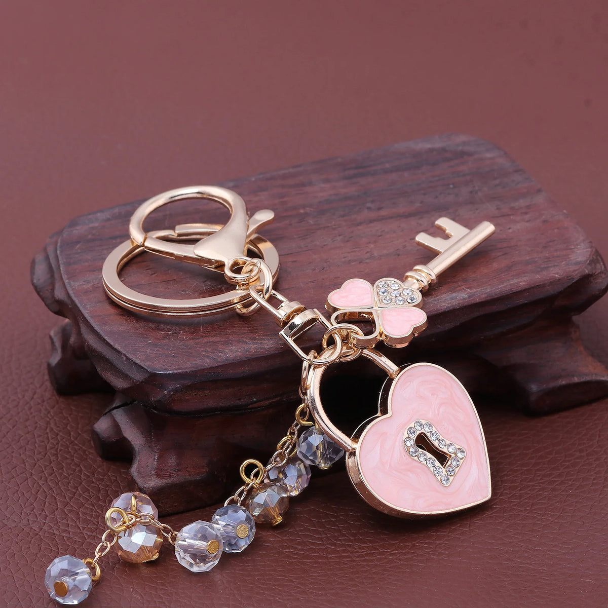Gold-toned keychain featuring a bow and heart charm with clear rhinestones on a dark wooden surface.
