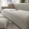 A light beige quilted stretch sofa cover with a textured weave and matching throw pillows on a modern sofa.