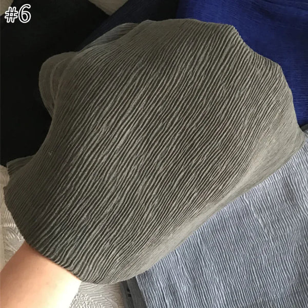 A close-up of a gray crinkle cotton scarf or shawl draped over a person's hand and arm.