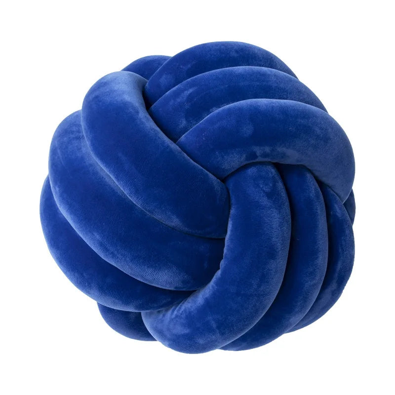 A deep blue velvet throw pillow with a tightly knotted, round design.