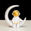 A white astronaut figurine with a gold helmet is displayed on a crescent moon shape.