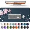 A waterproof PU leather desk pad featuring a laptop, keyboard, and mouse on a dark surface with pink cherry blossoms.