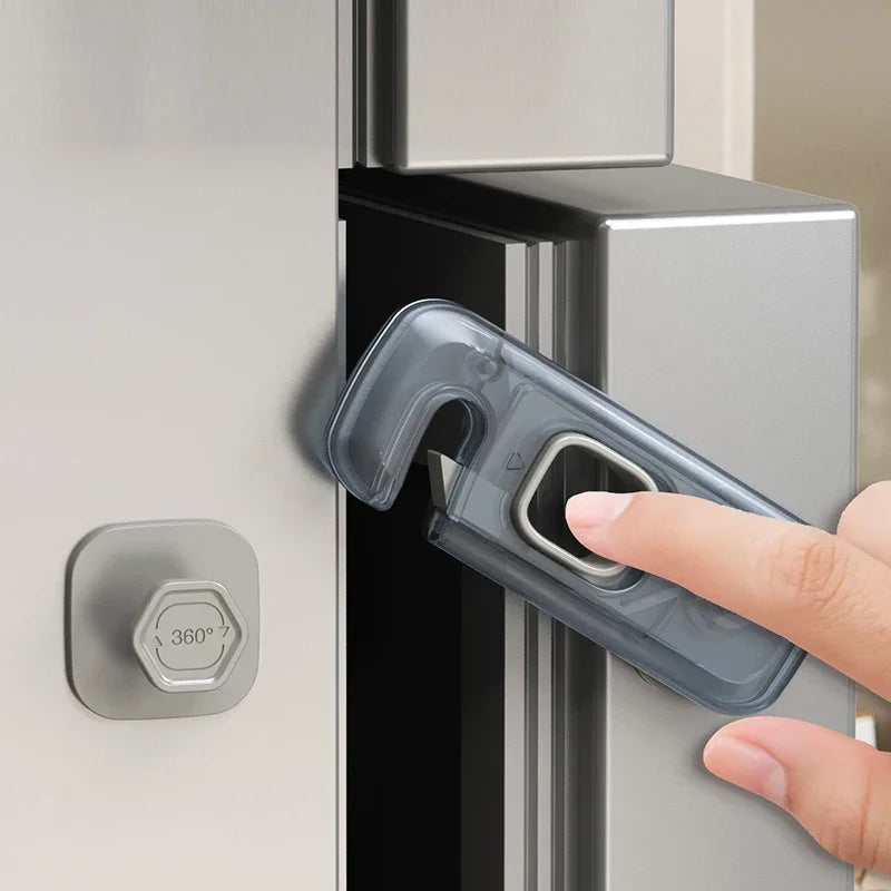 A hand is using a clear plastic lock to open a silver cabinet door, demonstrating a child safety mechanism.