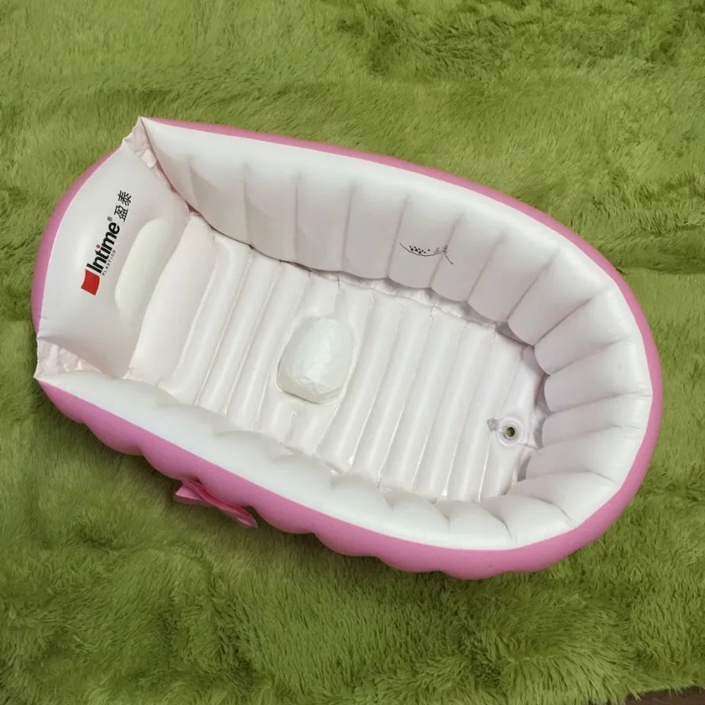 Pink inflatable bathtub for babies and toddlers with a hand pump resting on green fabric.