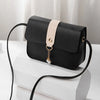 A black compact crossbody handbag with a light beige adjustable strap resting on a white surface.