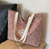 A pink corduroy tote bag with floral accents and light beige straps resting on a wooden surface.