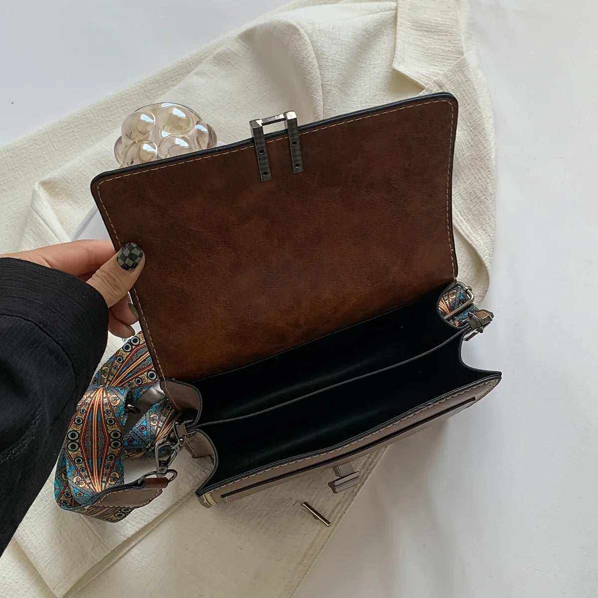 A brown leather mini cross-body bag with a silver clasp is shown against a white fabric background.