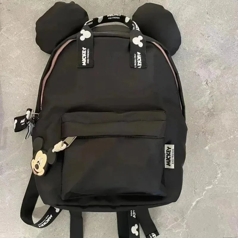 A black Mickey Mouse-themed backpack with a cow print design and a front pocket.