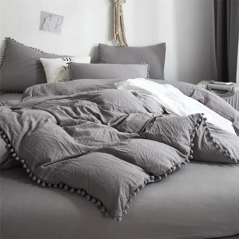 A gray duvet cover set with a pom-pom trim is displayed on a bed.