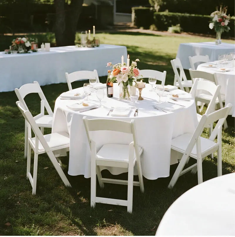 White elegant satin round tablecloth set up outdoors for a wedding or event.