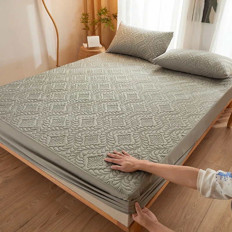 A hand is adjusting a gray quilted mattress protector with extra padding on a bed.