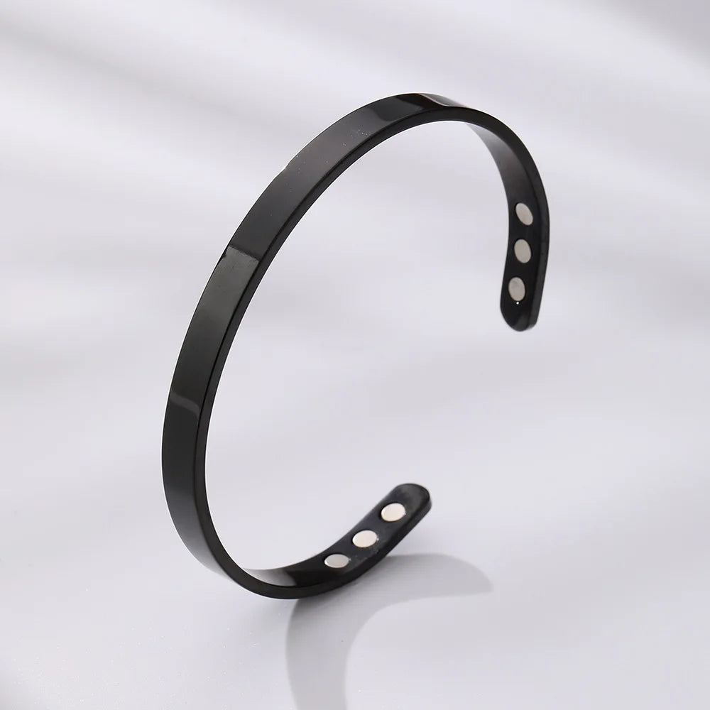 Bracelet manchette magnétique noir ajustable, présenté sur une surface gris clair.