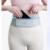 A woman wearing a light pink top and beige leggings demonstrates the Ultra-Thin Waterproof Running Waist Pack.