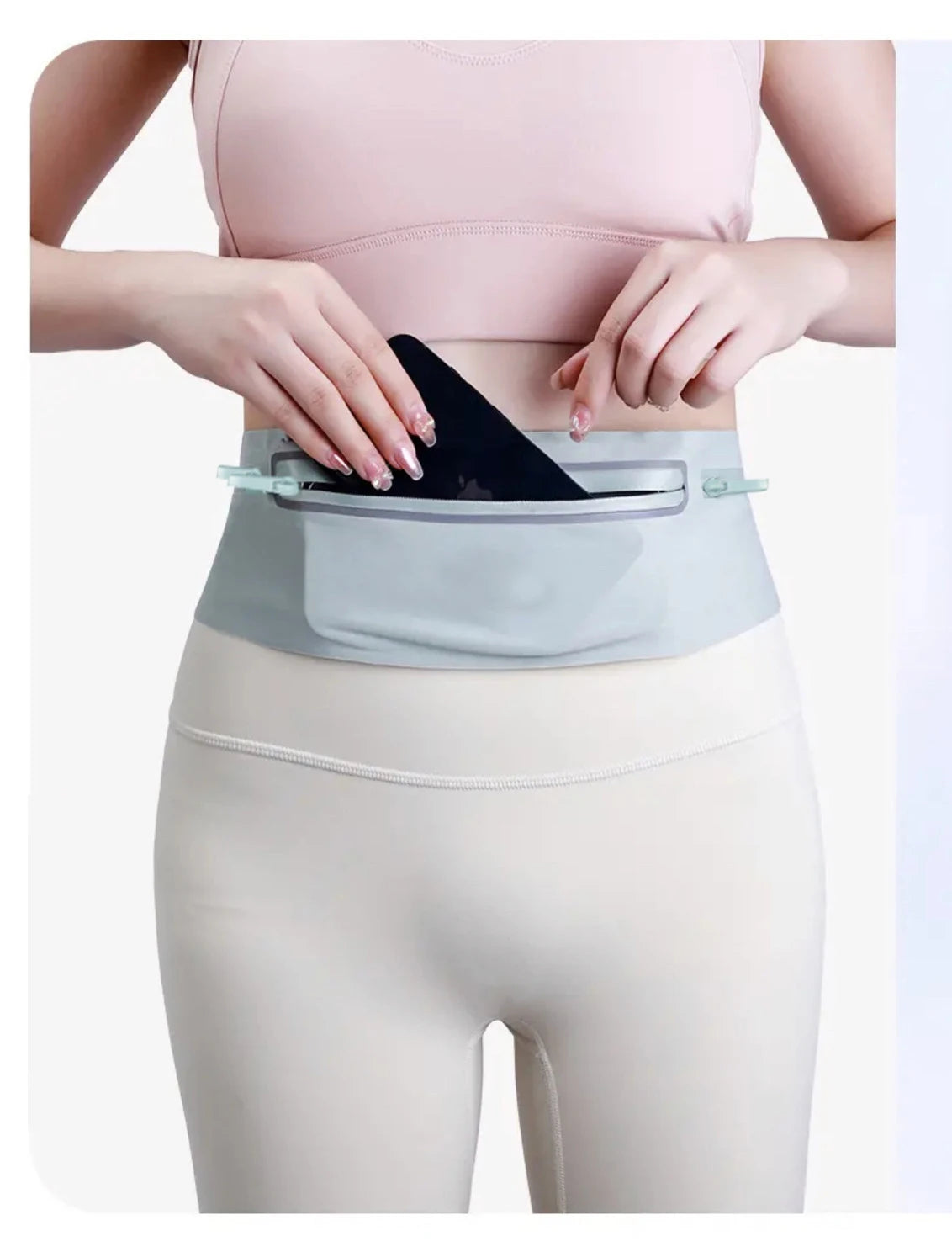 A woman wearing a light pink top and beige leggings demonstrates the Ultra-Thin Waterproof Running Waist Pack.