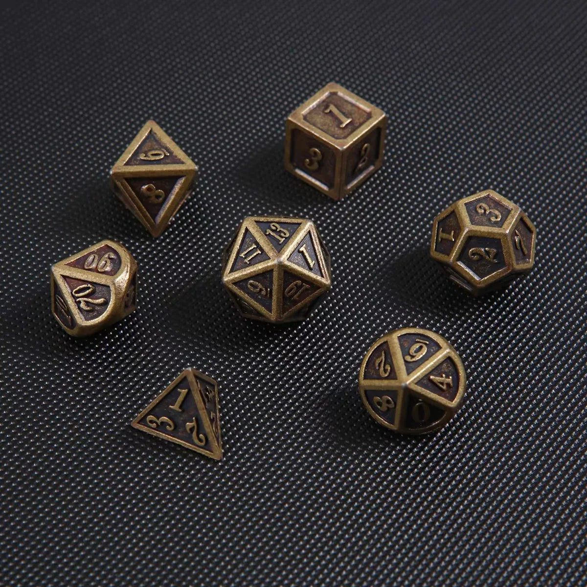 A collection of bronze metal polyhedral dice, including d6s and d10s, scattered on a dark surface.
