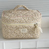 A beige floral quilted cosmetic bag with a light yellow zipper and fabric ribbon is displayed on a white shelf.