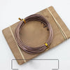 A coil of rose gold anodized aluminum jewelry wire resting on a wooden board.