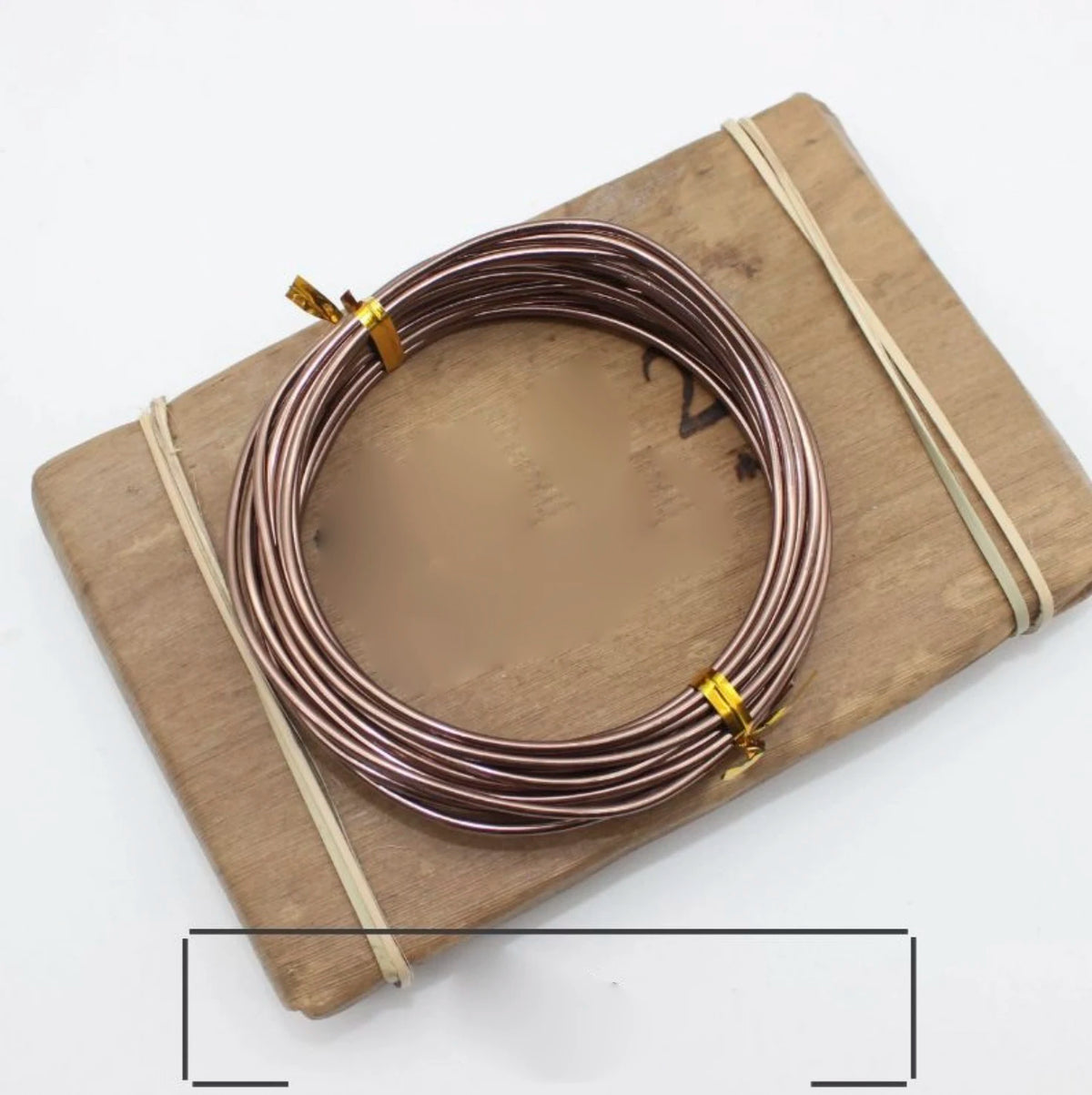 A coil of rose gold anodized aluminum jewelry wire resting on a wooden board.