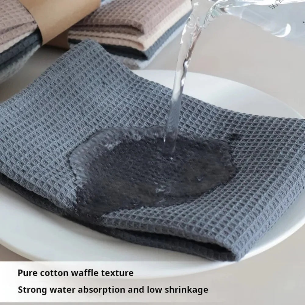 A close-up of a gray cotton waffle weave towel being used to absorb water on a white plate.