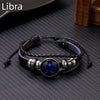 A black leather wrap bracelet featuring a glowing blue zodiac sign charm on a dark surface.