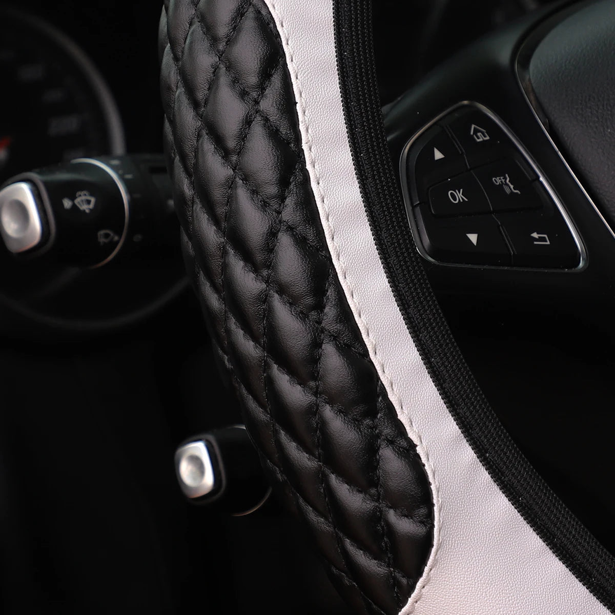 Close-up of a black quilted steering wheel cover with white piping and controls.