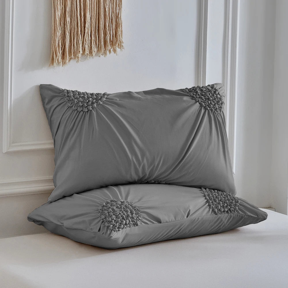 A gray duvet cover set with pleated fabric and floral embroidery resting on a white bed.