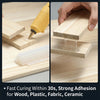 A hand applies a clear hot glue stick to a piece of wood, demonstrating strong adhesion for various materials.