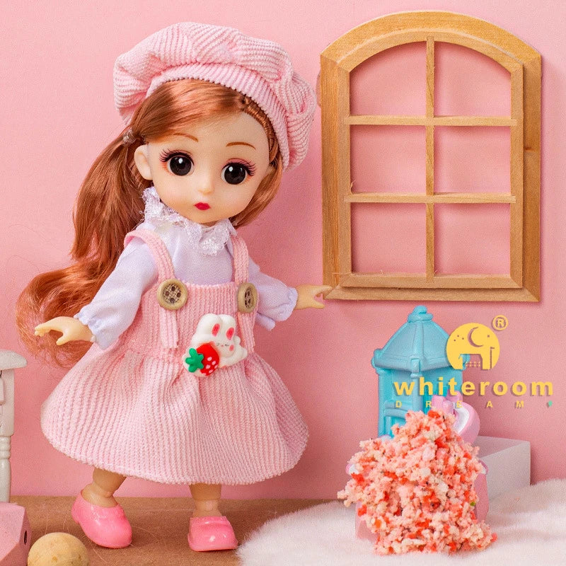 A pink fashion doll with long orange hair wearing a pink dress and apron standing in front of a wooden window.