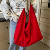 A bright red lightweight nylon tote bag is displayed hanging on a person's arm against a light gray hoodie and jeans.