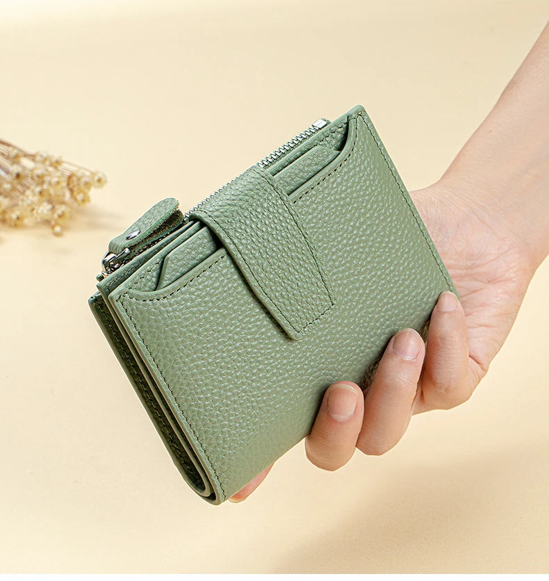 A hand holds a light green genuine leather RFID blocking bi-fold wallet with a zipper closure.
