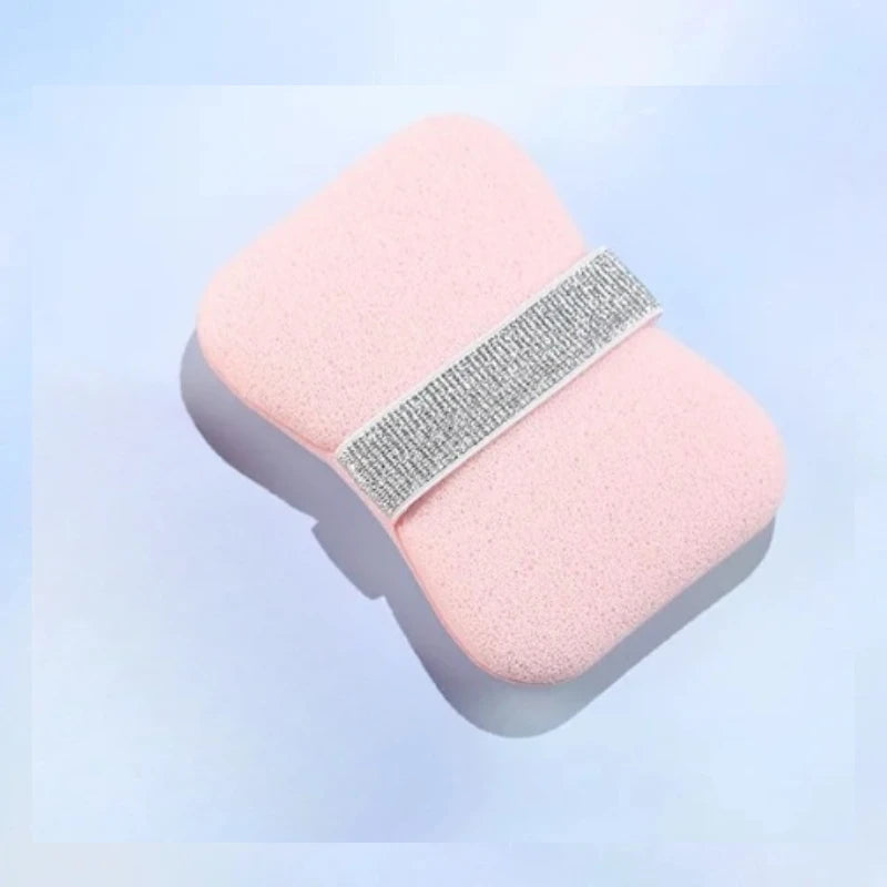 A pink foaming soap saver bag with a silver exfoliating mesh strip is shown against a light blue background.