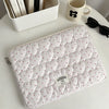 A quilted white laptop sleeve with a soft lining rests on a white table next to a mug and a box of books.