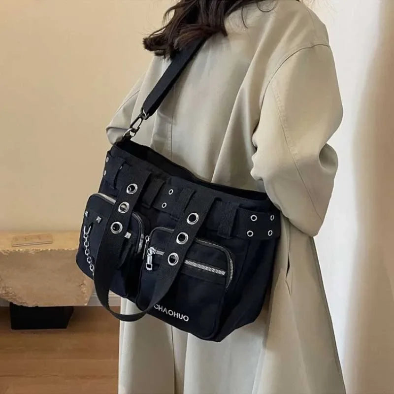 A black nylon shoulder bag with chain accents is worn by a person in a light beige coat.