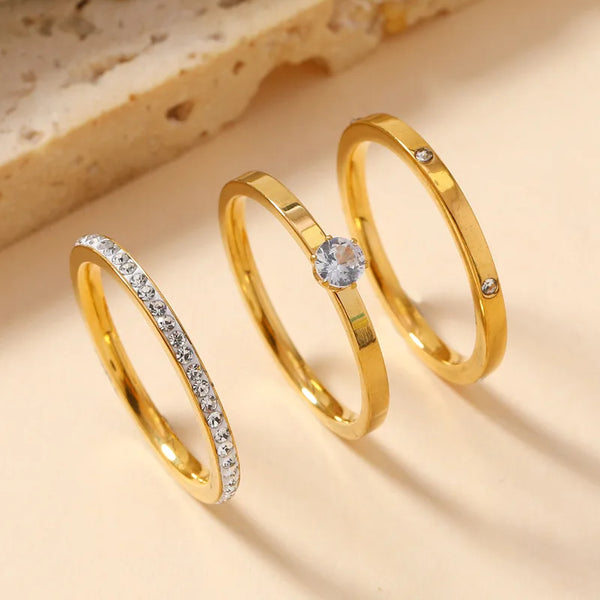 Ein Set aus drei goldfarbenen Ringen mit Zirkonsteinen auf hellem Hintergrund.