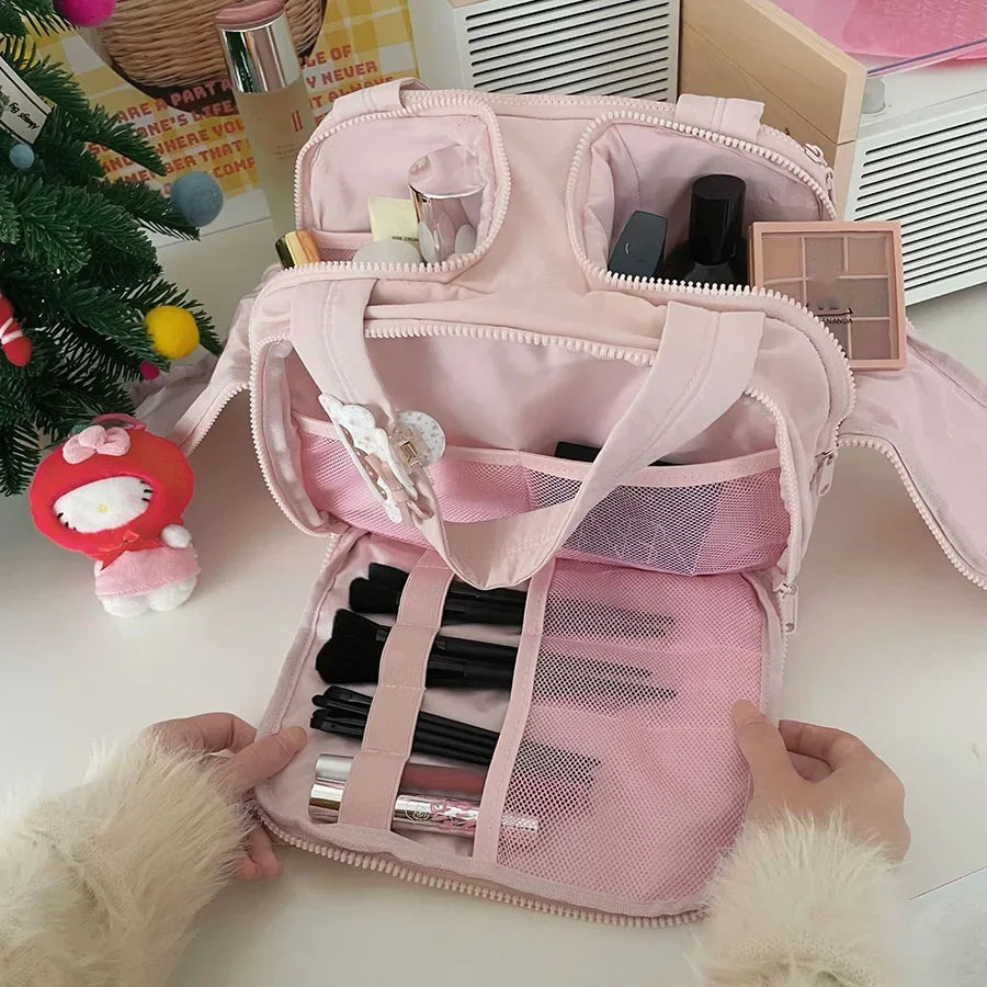 A pink cosmetic travel organizer with multiple compartments and a mesh pocket is shown being held by hands.