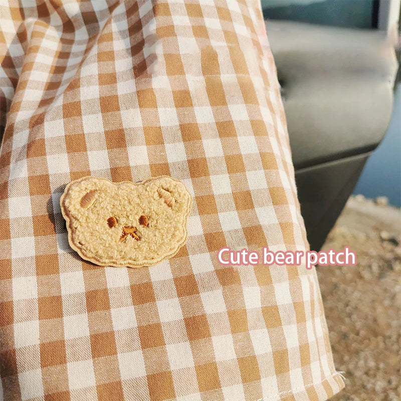 A cute bear patch is placed on a tan and white checkered fabric.