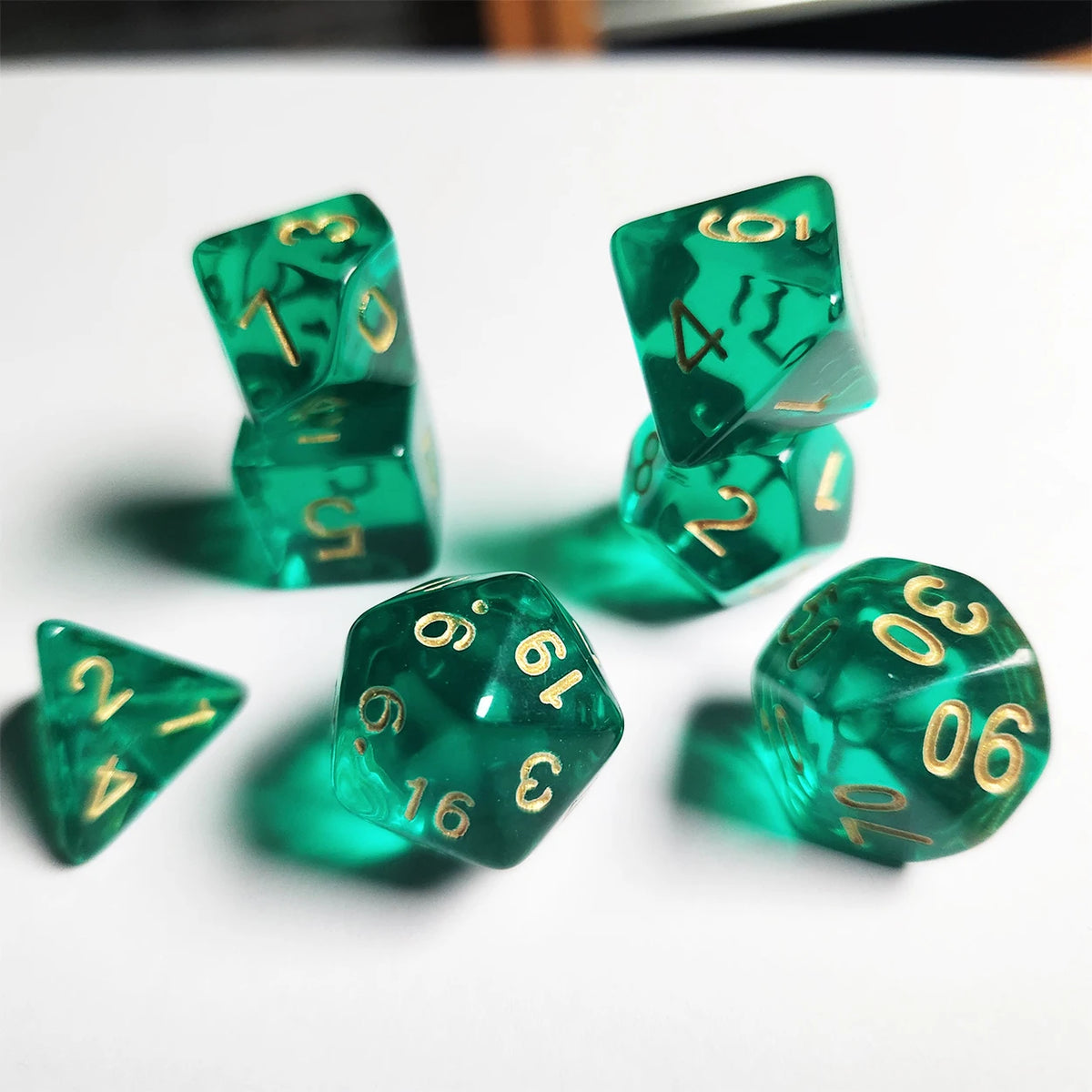 A set of seven translucent green acrylic polyhedral dice scattered on a white surface.