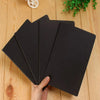 A stack of black A6 Kraft paper blank notebooks for sketching and journaling being held by a hand.