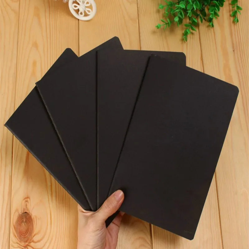 A stack of black A6 Kraft paper blank notebooks for sketching and journaling being held by a hand.