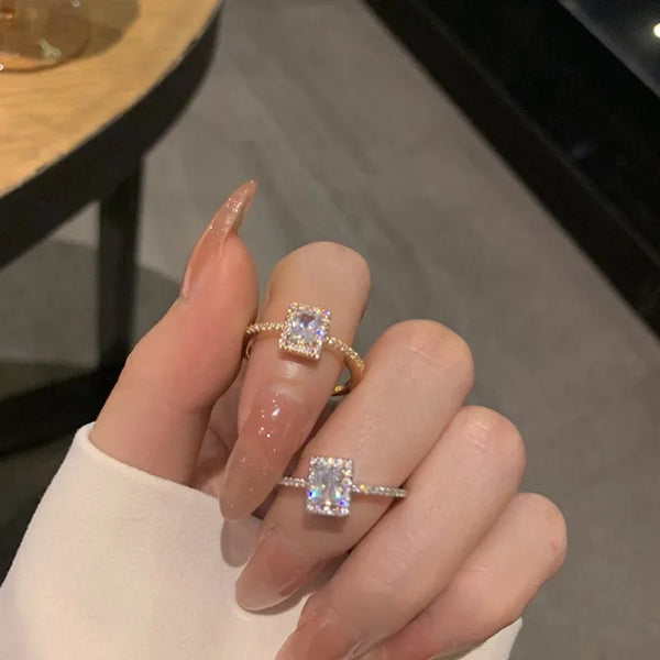 Una mano sostiene un anillo con un diseño geométrico de zirconia clásico en una banda ajustable abierta.