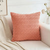 A square, textured coral pink corduroy pillow with a woven striped velvet design resting on a white surface.