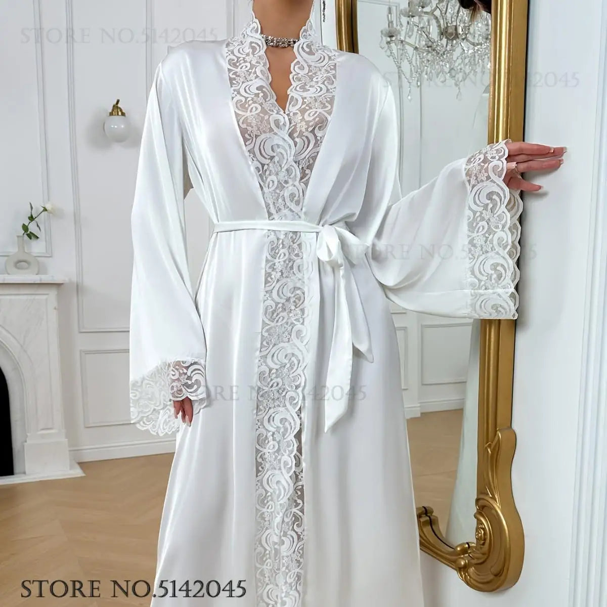 A white silk satin robe with intricate lace trim is displayed hanging on a golden mirror.