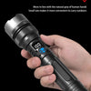 A hand holds a black high-power rechargeable LED flashlight with a digital display, demonstrating its one-handed grip.