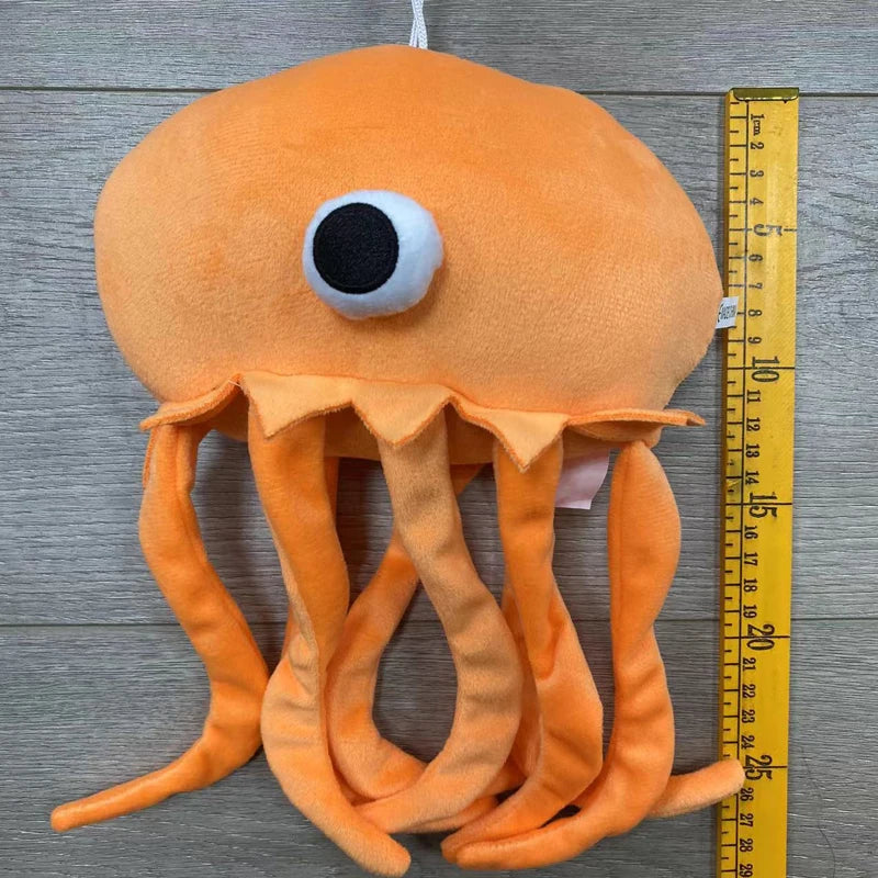 An orange plush toy resembling an octopus with tentacles, photographed next to a ruler.