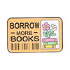 An enamel pin featuring the text BORROW MORE BOOKS on a rectangular yellow background with a floral design.