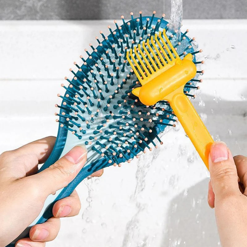 Hands are rinsing a blue dual-sided hairbrush with yellow rake teeth under running water.