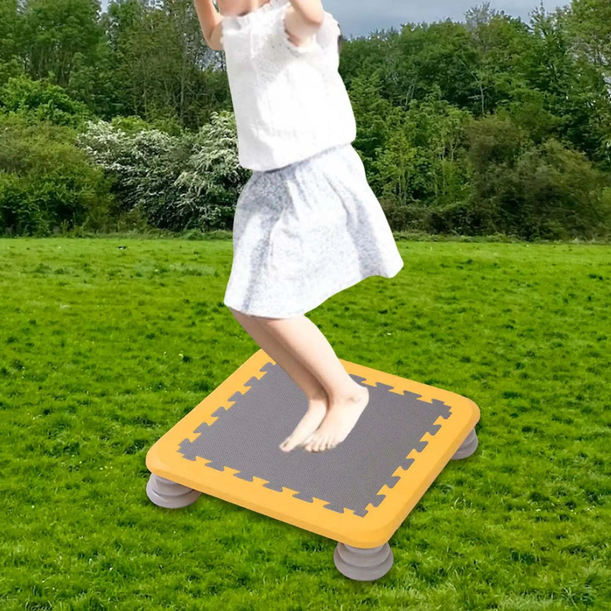 A child is standing on a yellow mini trampoline mat outdoors in a grassy field.